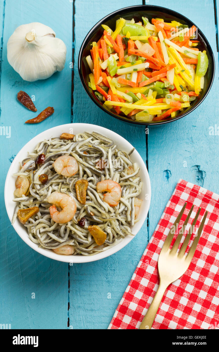 Surimi Glasaale mit Garnelen, Knoblauch und Pfeffer auf einer weißen Schüssel und Gemüse auf einer schwarzen Schale Stockfoto