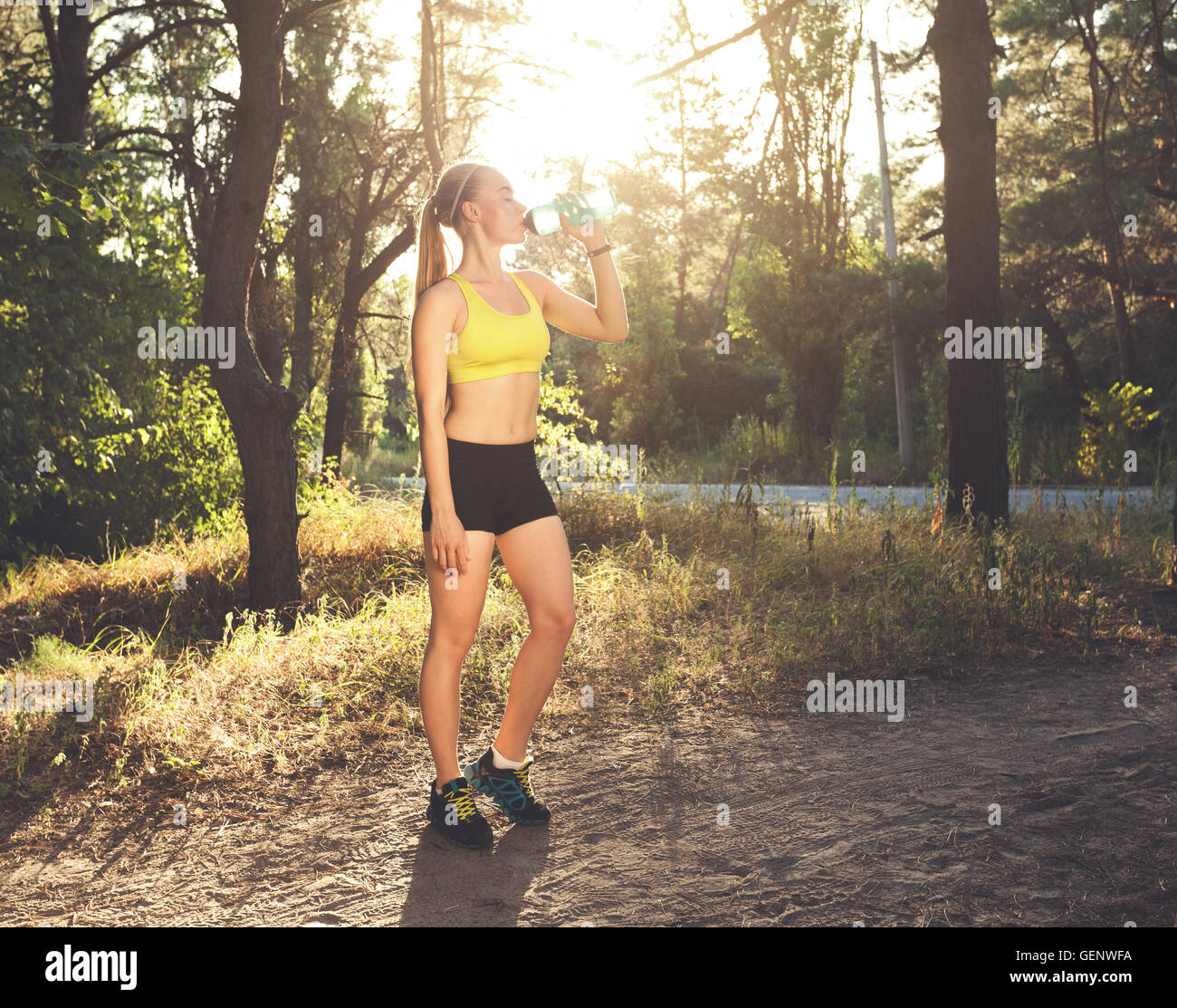 Junge Sportlerin Trinkwasser nach laufen, Sportübungen, Fitness. Schöne sportliche Mädchen ruhen bei Sonnenuntergang im Sommer Wald. Stockfoto