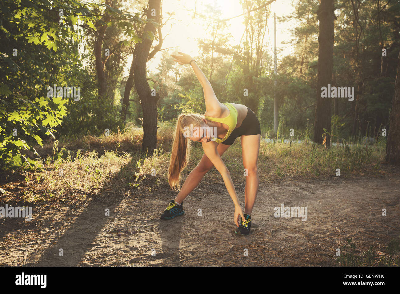 Junge Sportlerin dehnen. Schöne sportliches Mädchen Übungen im Wald bei farbenfrohen Sonnenuntergang im Sommer abends sport. Fitness Stockfoto