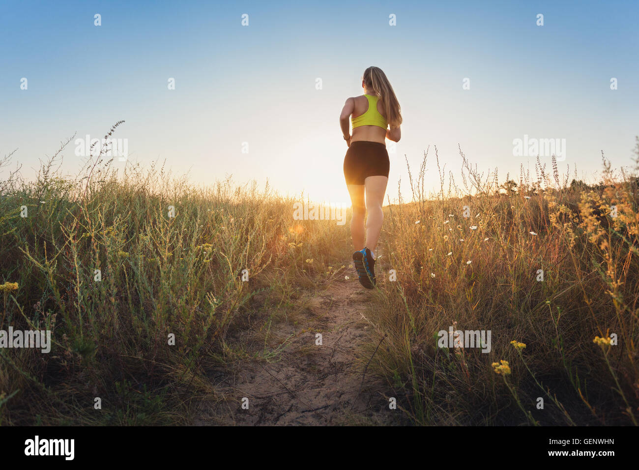 Sportliche Mädchen laufen auf einer Landstraße bei Sonnenuntergang in Sommerwiese. Athlet läuft auf der off-Road am Abend. Gesund Stockfoto