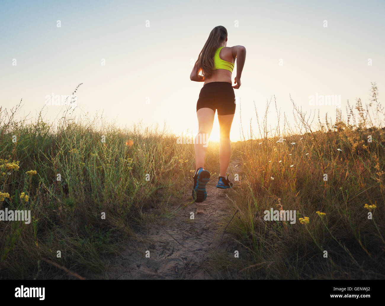 Sportliche Mädchen laufen auf einer Landstraße bei Sonnenuntergang in Sommerwiese. Athlet läuft auf der off-Road am Abend. Gesund Stockfoto