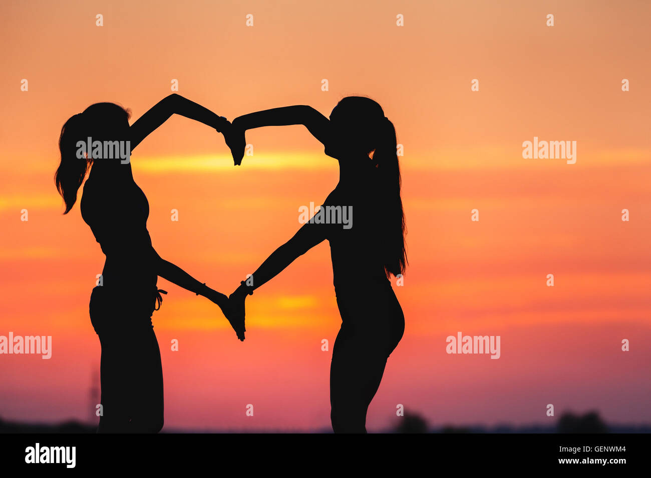 Landschaft mit Silhouette der junge sportliche Frauen Hand in Hand in Herzform auf dem Hintergrund der bunten Himmel bei Sonnenuntergang in summ Stockfoto