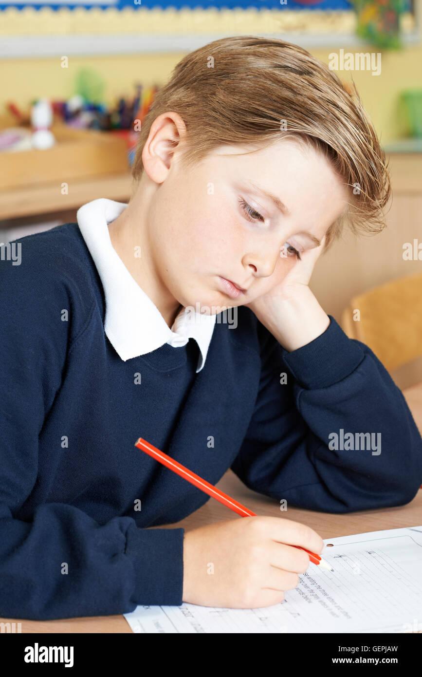 Gelangweilt männlichen Grundschule Schüler am Schreibtisch Stockfoto