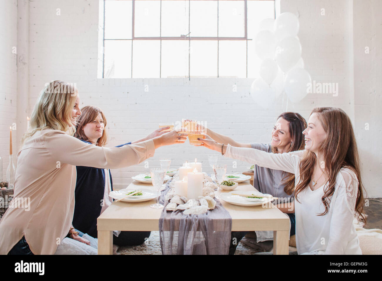 Vier Frauen sitzen an einem niedrigen Tisch, heben ihre Gläser in einem Toast auf einander. Stockfoto