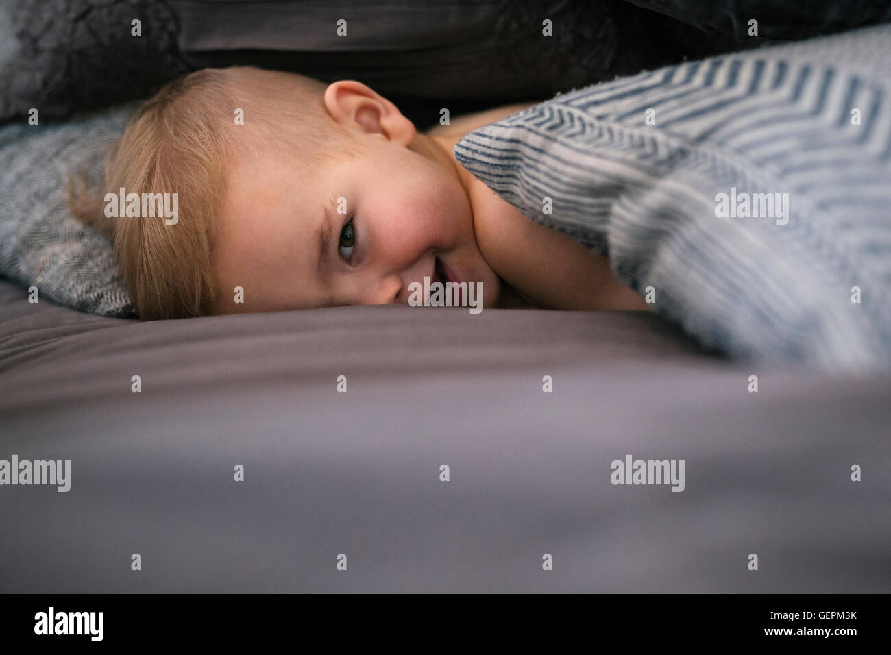 Ein kleiner Junge, liegend auf dem Bauch im Bett in die Kamera schaut und lacht. Stockfoto