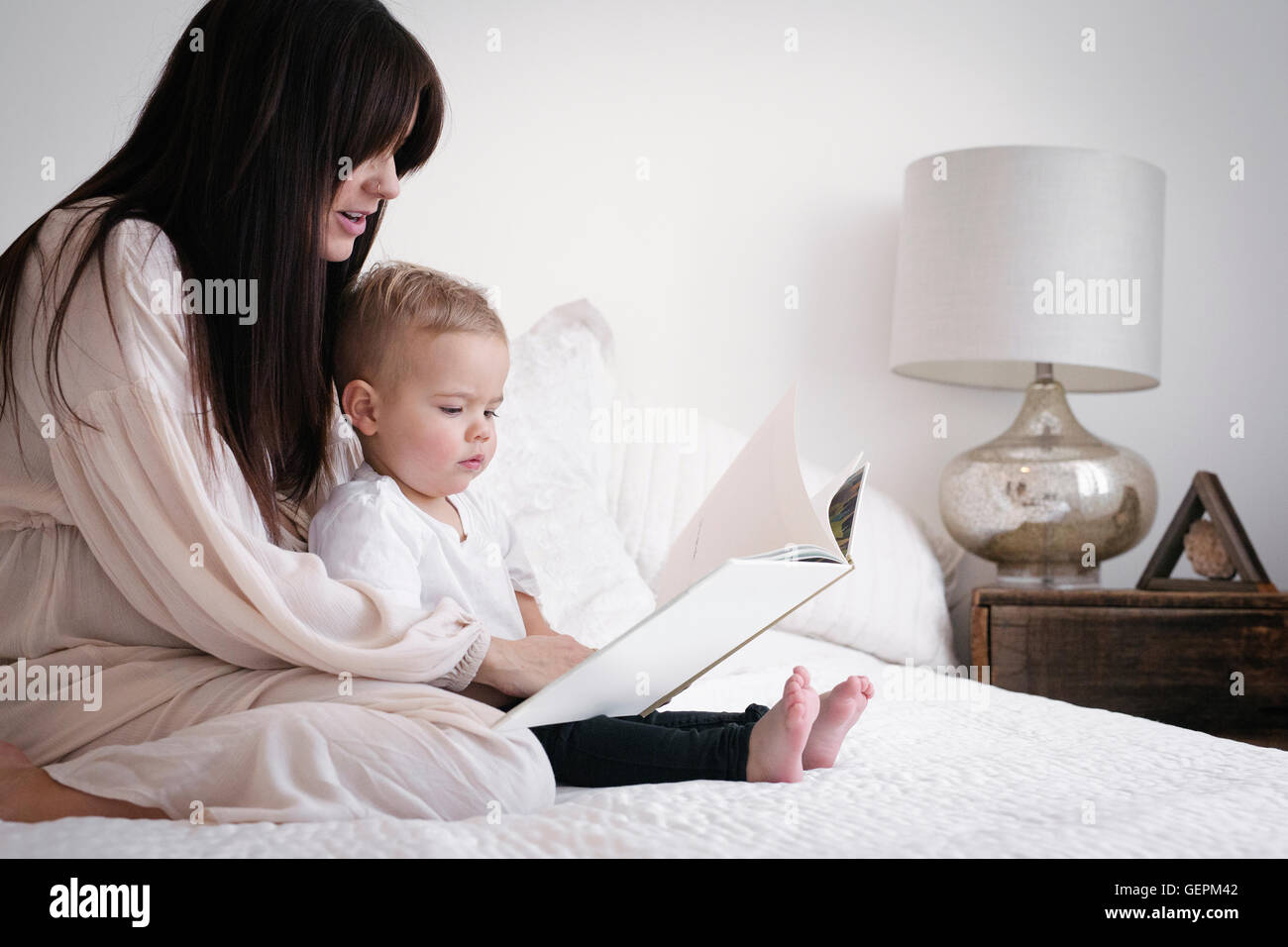 Eine hochschwangere Frau spielt mit ihrem kleinen Sohn. Sitzen auf einem Bett, eine Geschichte zu lesen. Stockfoto