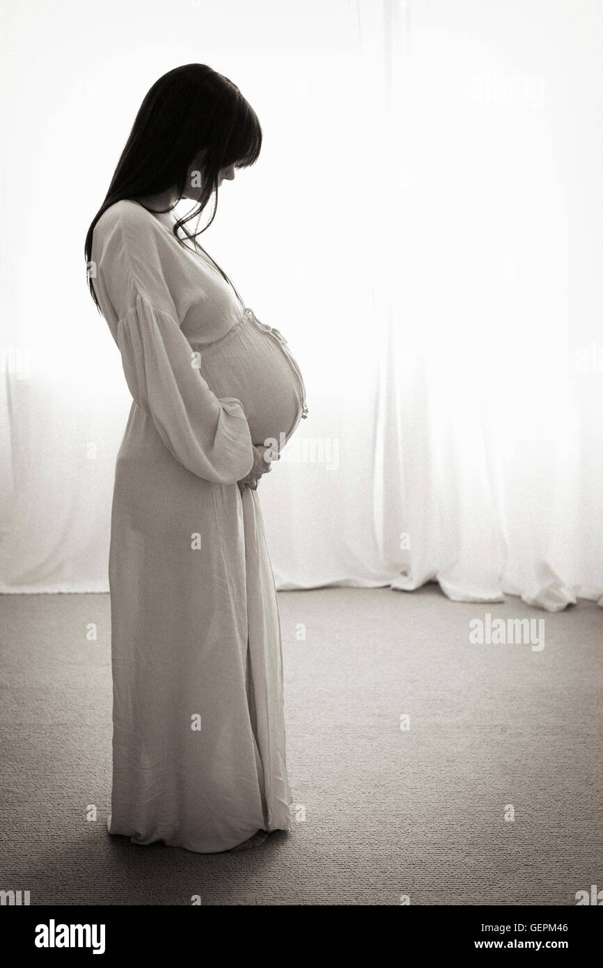 Eine hochschwangere Frau mit ihren Händen auf dem Bauch, im Profil gesehen. Stockfoto