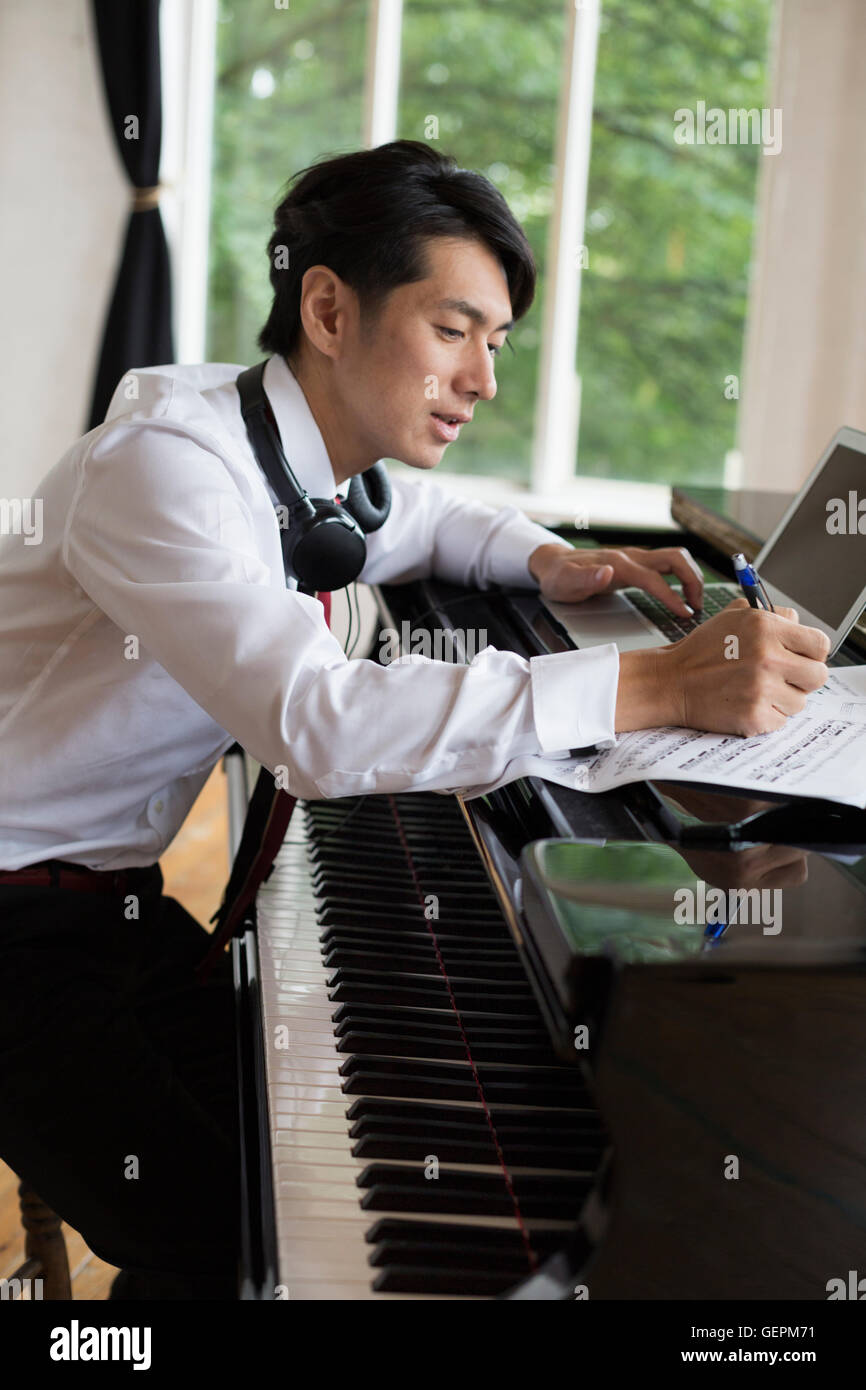 Junger Mann sitzt an einem Flügel in einem Proberaum kommentieren Noten. Stockfoto