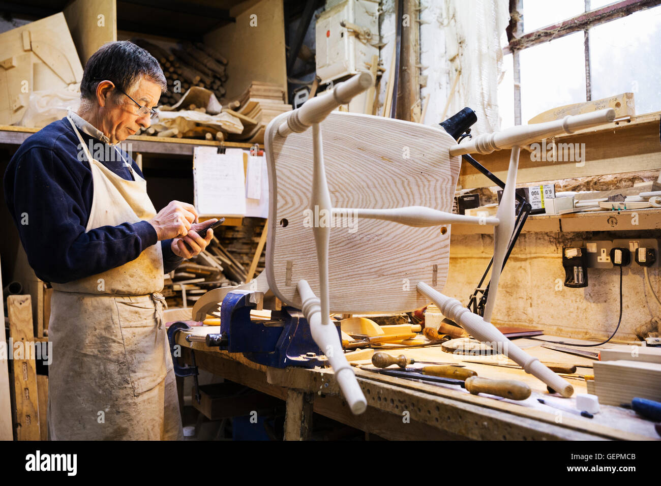 Mann, stehend auf einer Werkbank in einer Tischlerei, arbeiten auf einem Holzstuhl. Stockfoto