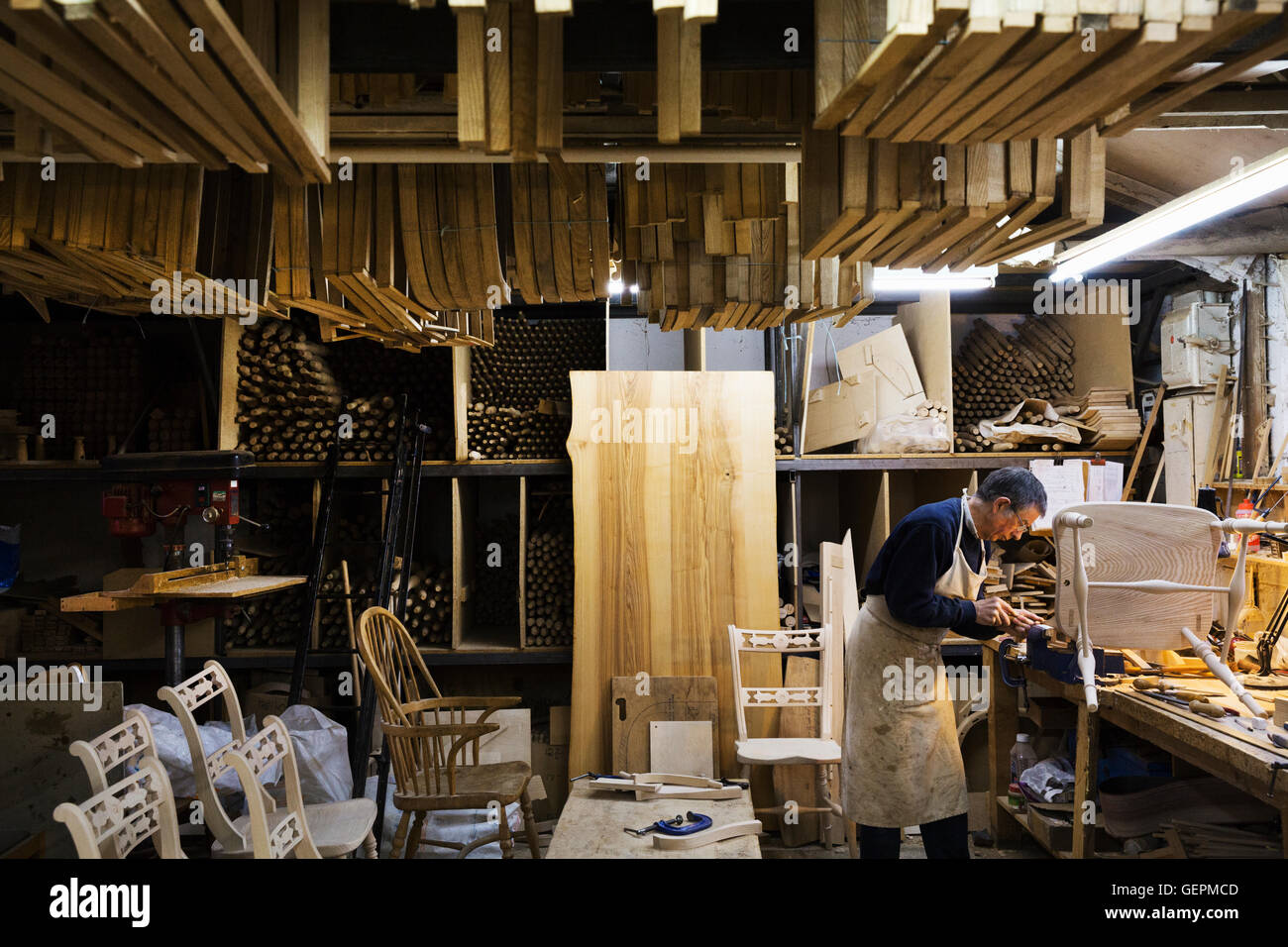 Mann, stehend auf einer Werkbank in einer Tischlerei, arbeiten auf einem Holzstuhl. Stockfoto