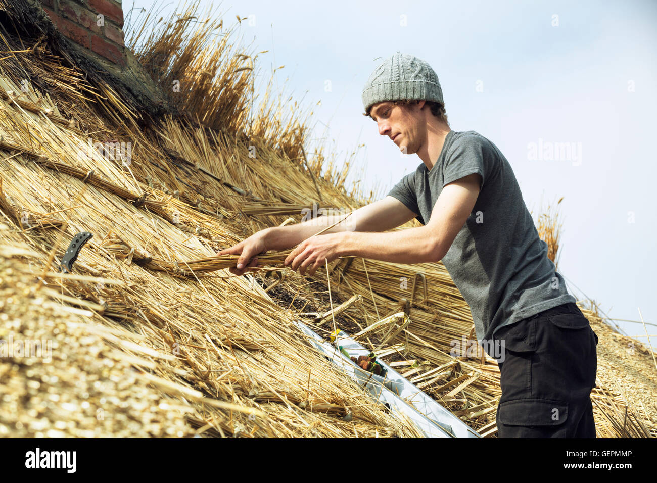 Junger Mann thatching Dach, auf einer Leiter stehend. Stockfoto