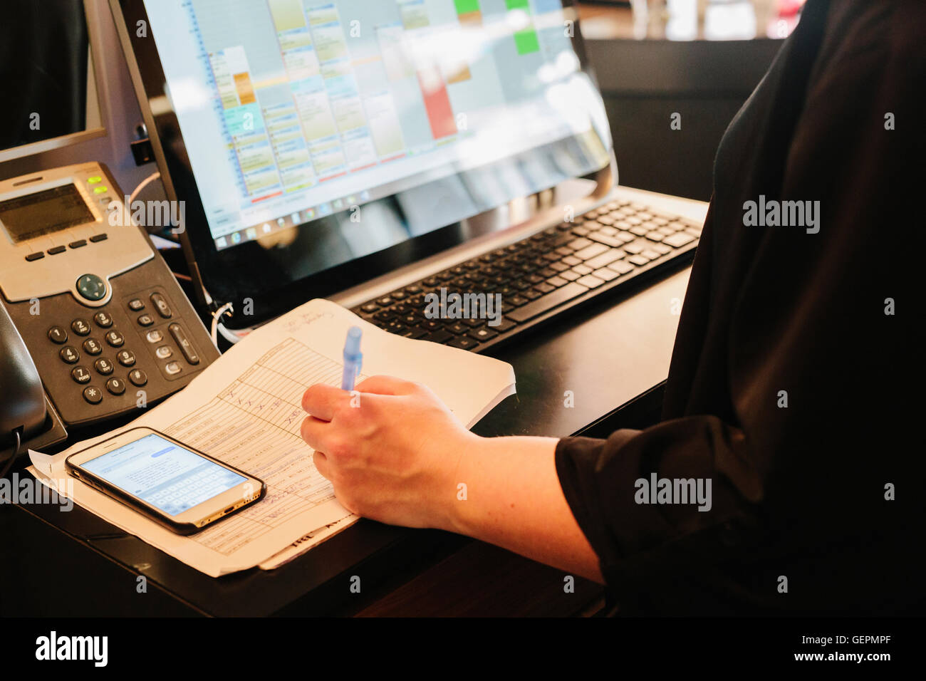 Eine Person arbeitet an einem Haar Salon Rezeption, Laptop-Computer, Festnetz-Telefon, Tagebuch und Smartphone auf dem Schreibtisch. Stockfoto