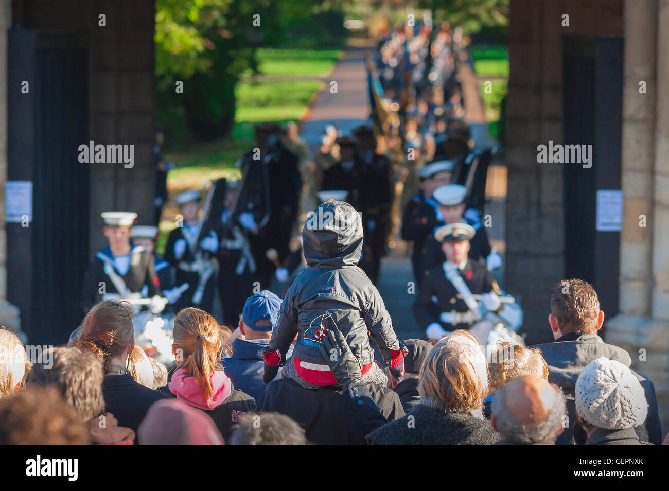 Kind auf den Schultern sitzt ein Kind auf den Schultern seines Vaters, um am Remembrance Day in Bury St Edmunds, Suffolk, Großbritannien, einen besseren Blick auf eine Marinekapelle zu bekommen. Stockfoto