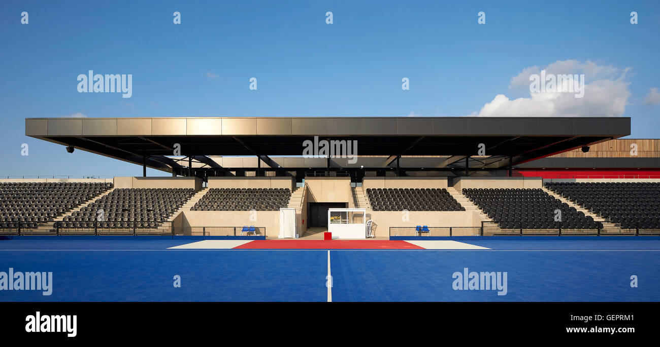Frontalansicht des Hockeyfeld in blau mit Zuschauertribüne. Eton Manor - Lee Valley Hockey und Tennis Centre, London, Vereinigtes Königreich. Architekt: Stanton Williams, 2014. Stockfoto