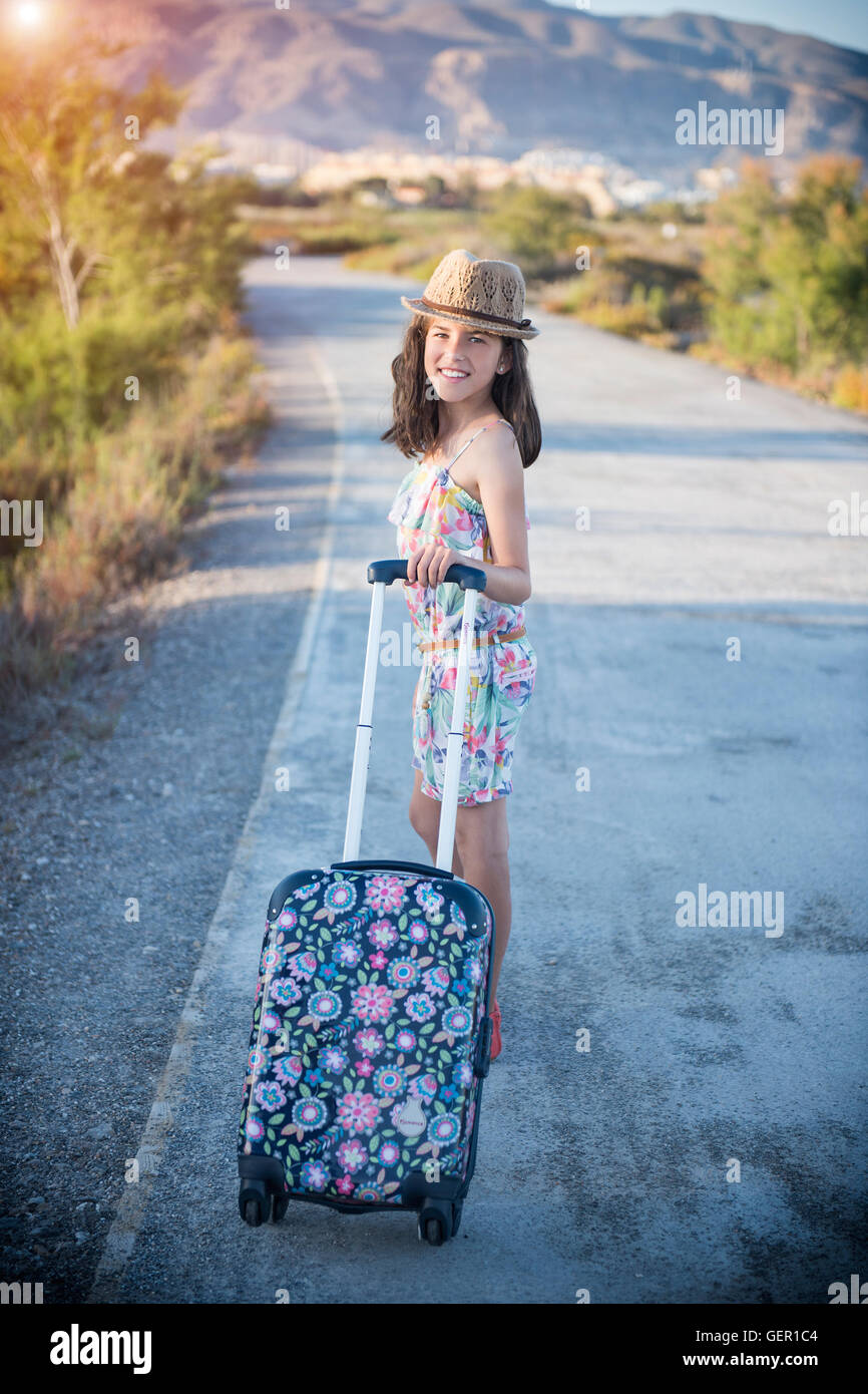 Schöne fröhliche junge Mädchen mit einem Koffer zu Fuß entlang der Straße Stockfoto