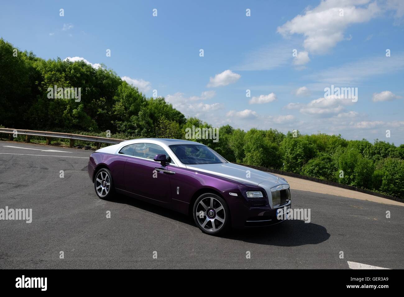 Ein Rolls-Royce Wraith Coupé steht auf eine Asphaltstraße an der Spitze eines Hügels mit Bäumen und Sommerhimmel hinter Stockfoto