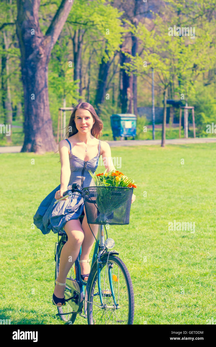 Schöne junge Frau auf Fahrrad mit Blume im park Stockfoto