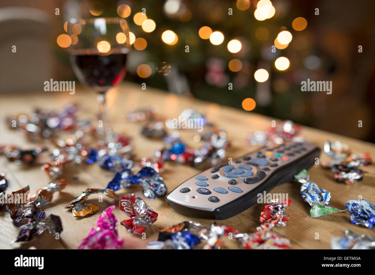 TV-Fernbedienung umgeben von Bonbonverpackungen und ein Glas Rotwein zu Weihnachten. Stockfoto
