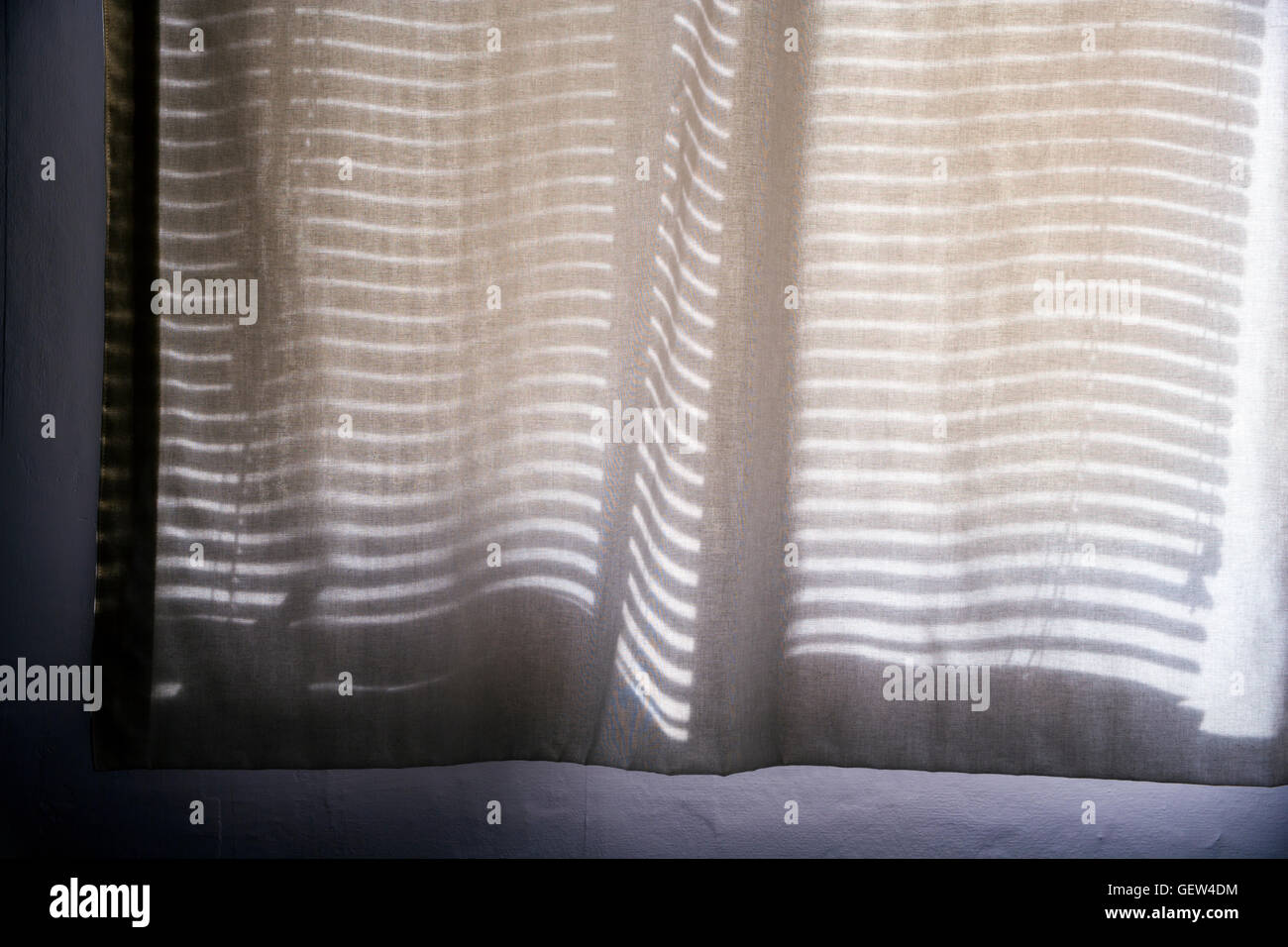 Horizontal-Jalousien werfen eine Muster von Schatten auf eine transparente Baumwolle Vorhang. Stockfoto