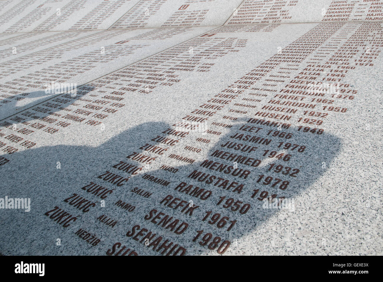Die Menschen werfen Schatten über die Wand der Opfernamen auf dem Srebrenica Potocari Genozid-Denkmal und Friedhof für die Opfer des 1995 Genozids im östlichsten Teil der Republika Srpska, einer Einheit von Bosnien und Herzegowina. Mehr als 8,000 bosnisch-muslimische Männer und Jungen wurden getötet, nachdem die serbische Armee am 10-11. Juli 1995 trotz der Anwesenheit von UN-Friedenstruppen Srebrenica, ein ausgewiesenes UN-Sicherheitsgebiet, angegriffen hatte. Stockfoto
