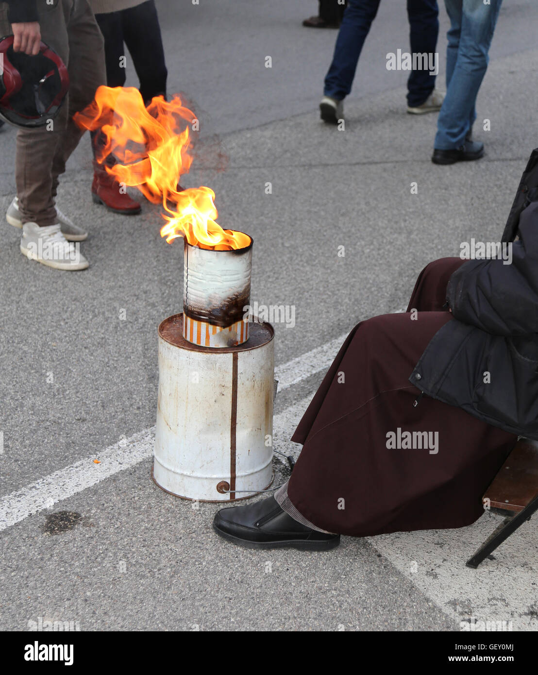 Armen Mönch mit braunen Kleid erwärmt sich vor das Feuer an einem Lagerplatz auf der Straße Stockfoto