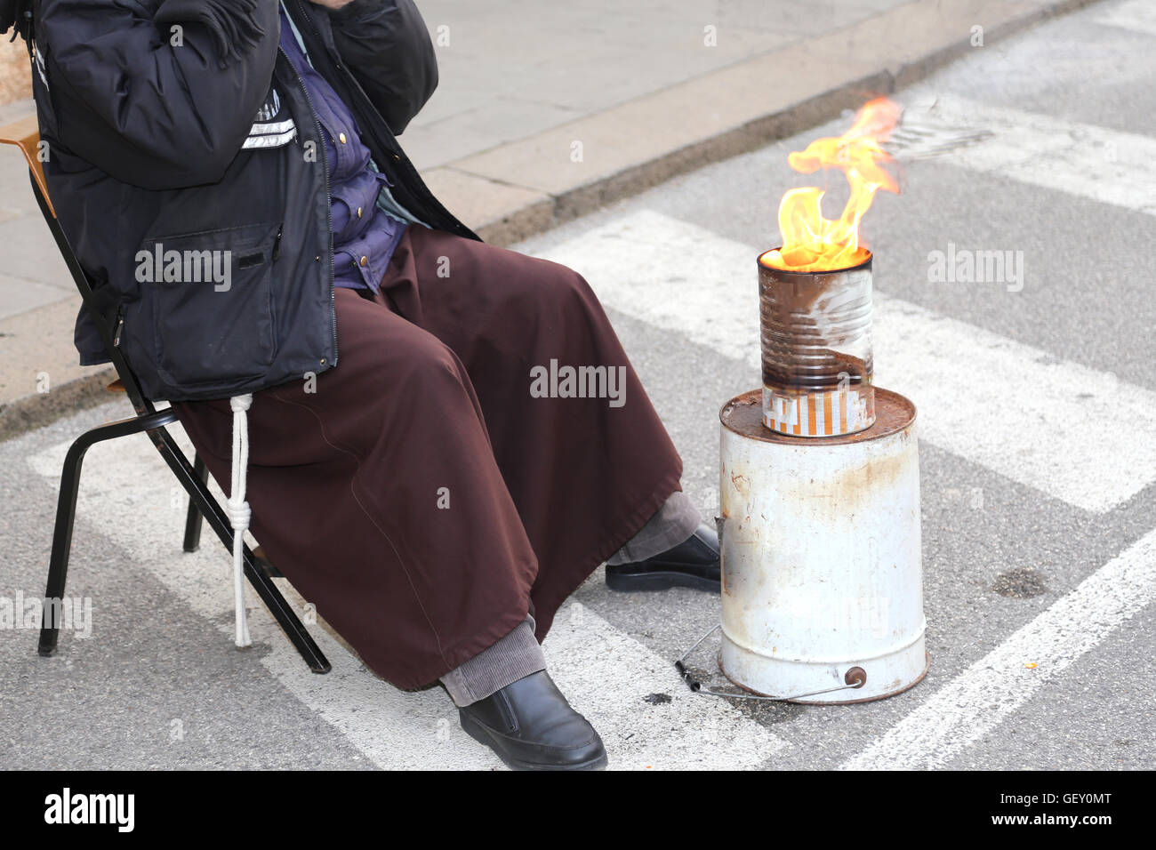 Armen Mönch mit braunen Kleid erwärmt sich vor das Feuer an einem Lagerplatz in der Straße im winter Stockfoto