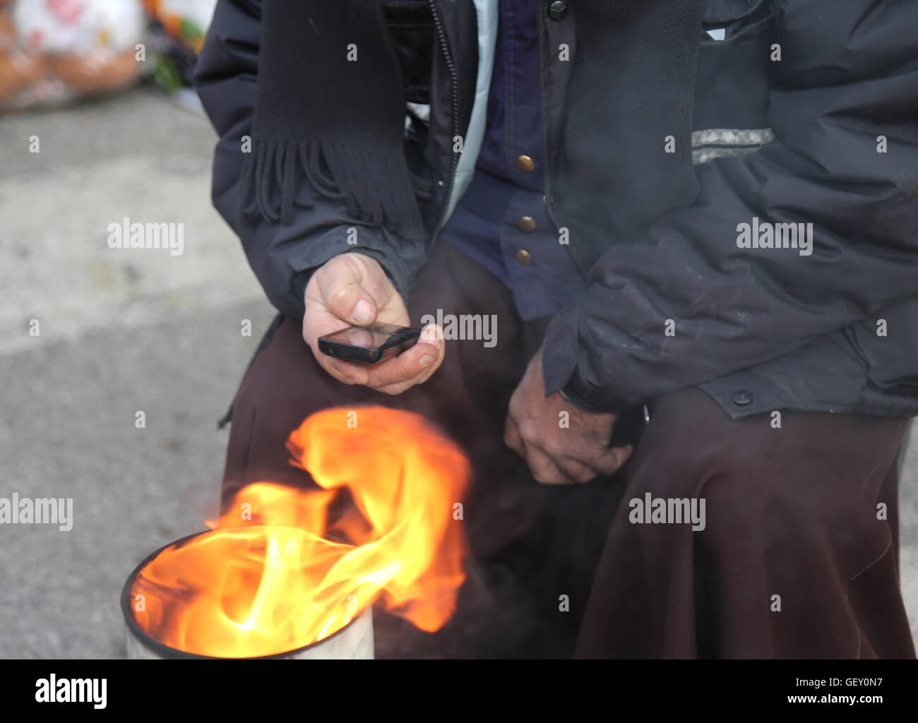 Armen auf der Straße mit Hilfe eines Mobiltelefons und heizt mit Lagerfeuer in einem Lagerplatz Stockfoto