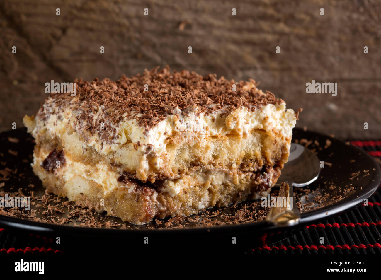 Tiramisu-Kuchen und Löffel auf dunklen Teller mit hölzernen Hintergrund Stockfoto