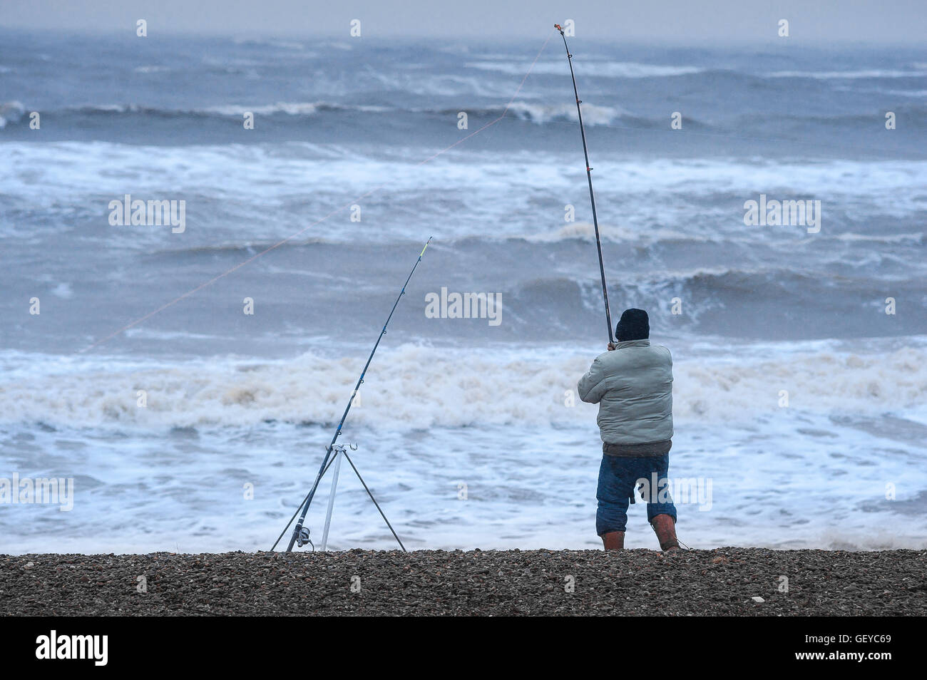 Mann fischt Meer stürmisches Wetter, Rückansicht eines Mannes, der vom Strand aus bei rauem Wetter in Dunwich an der Küste von Suffolk, England, fischt. Stockfoto