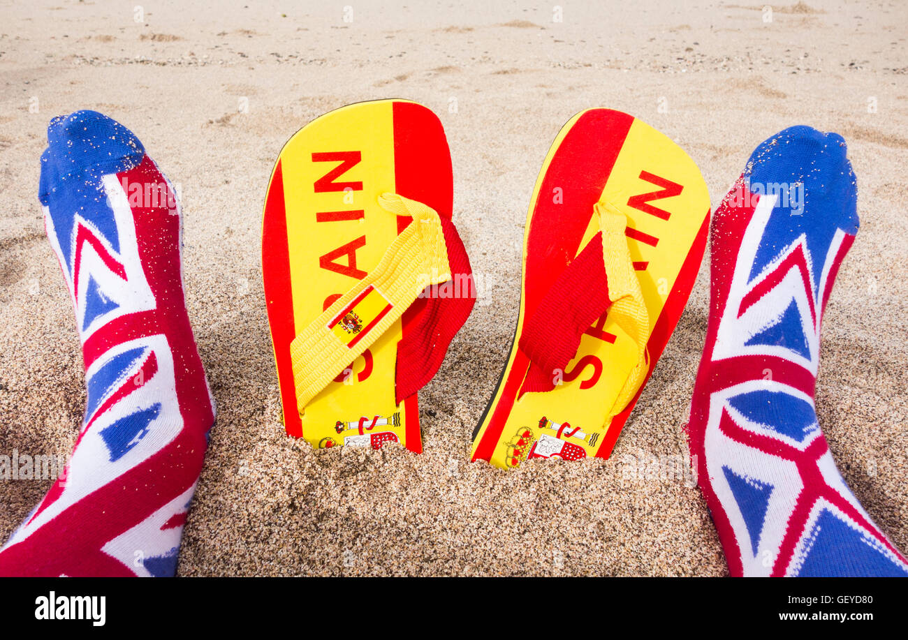 Britischer Tourist mit Union Jack Socken am Strand: Flip Flops mit spanischer Flagge im Sand. Brexit, Reisebeschränkungen, Freizügigkeit, EU Stockfoto