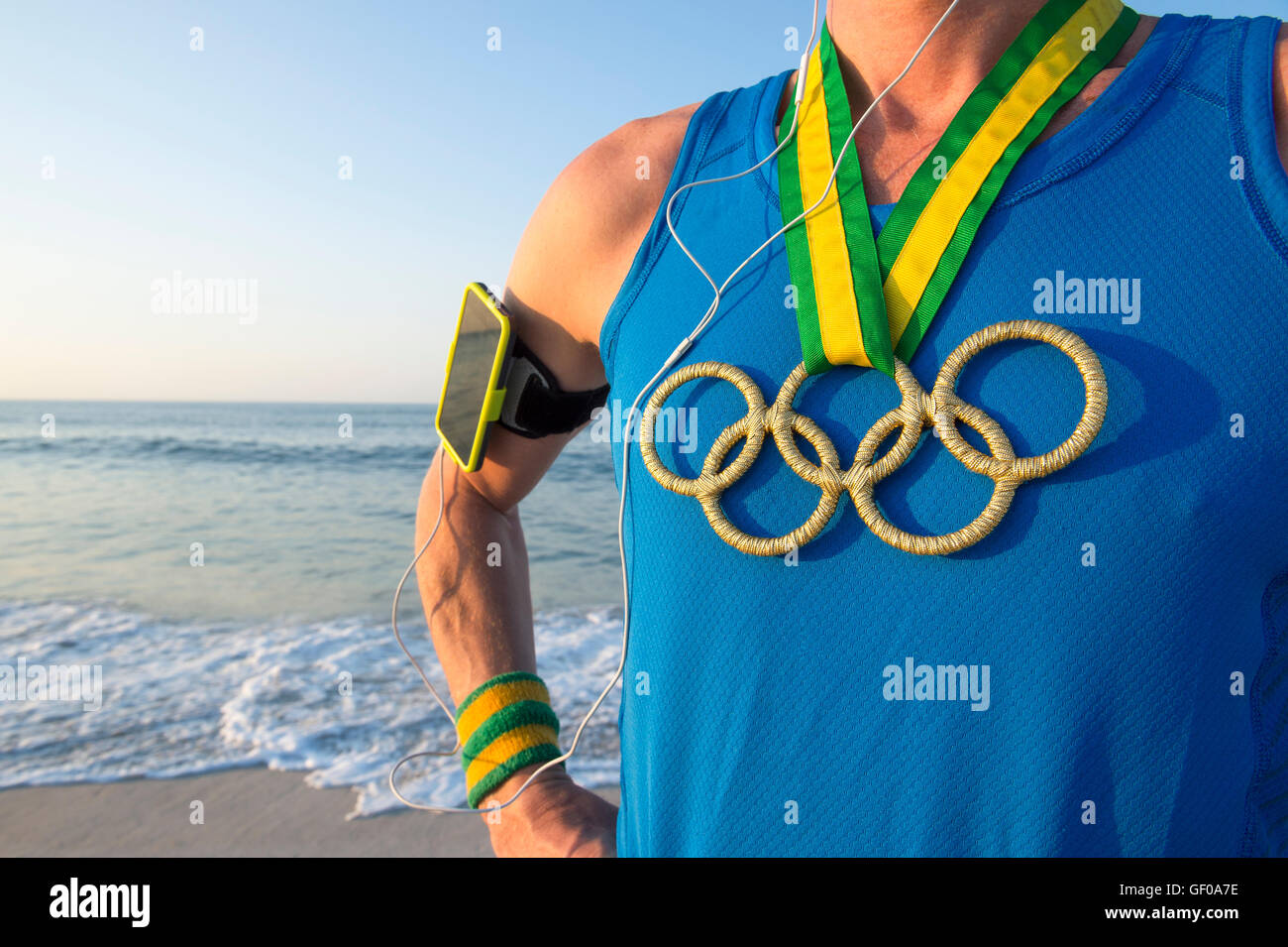 RIO DE JANEIRO - 10. März 2016: Sportler der Olympischen Ringe gold Medaillen und Sport Armband steht an einem Sonnenaufgang Strand tragen. Stockfoto