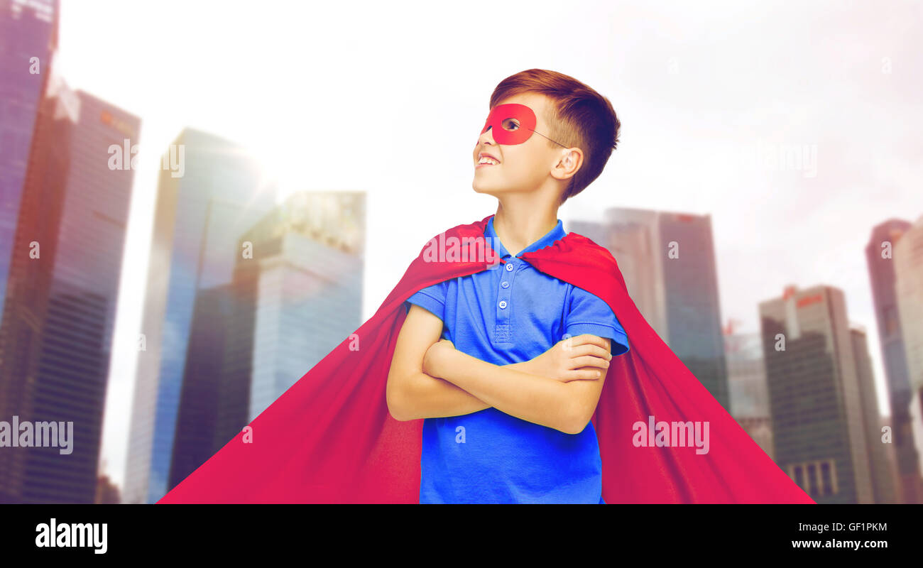 Junge im roten Superhelden Cape und Maske über Stadt Stockfoto