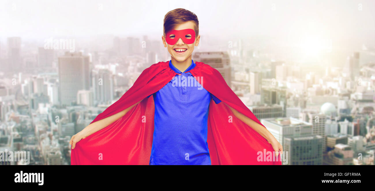 Junge im roten Superhelden Cape und Maske über Stadt Stockfoto