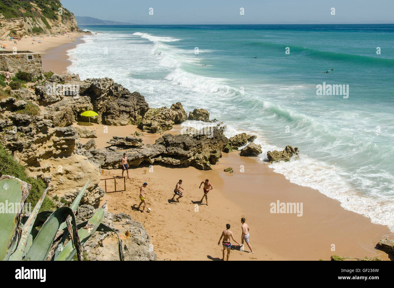 Junge Männer spielen Fußball auf einem Strand in der kleinen Küstenstadt von Los Caños de Meca, in der Provinz Cádiz. Einige Surfer warten auf Welle Stockfoto