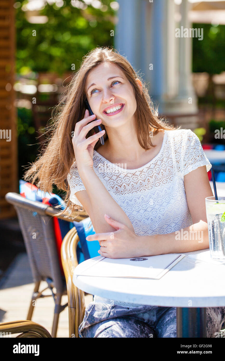 Glücklich Brünette Frau anrufen per Telefon im Open-Air-café Stockfoto