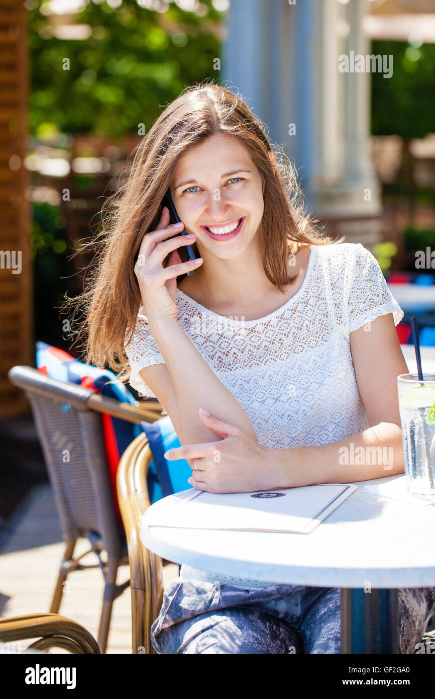Glücklich Brünette Frau anrufen per Telefon im Open-Air-café Stockfoto