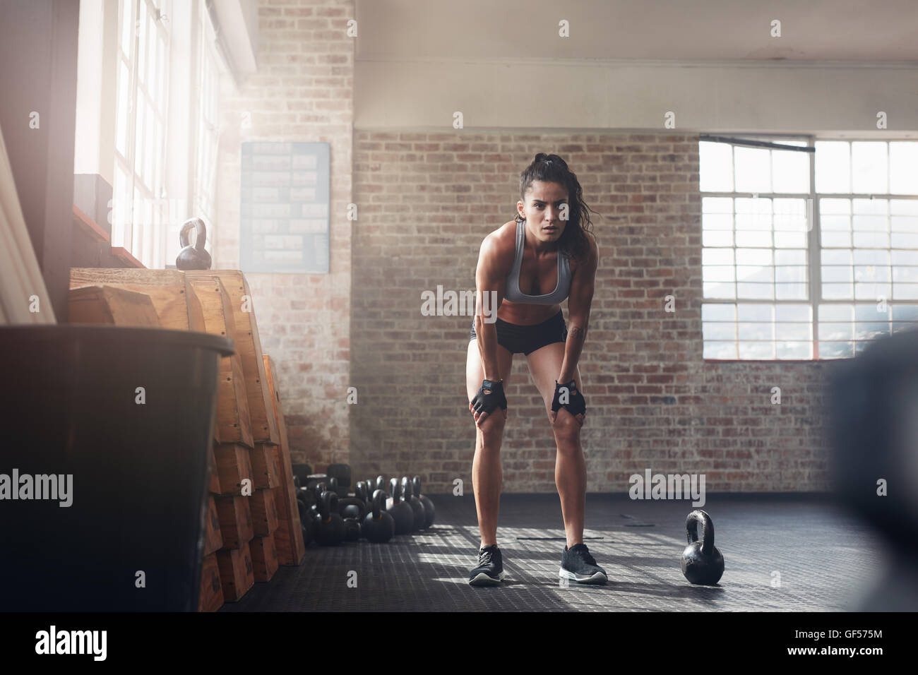 Voller Länge Schuss der selbstbewusste junge Frau bei Crossfit Gym. Muskulöse Sportlerin stehen mit ihr die Hände auf Knien suchen konzentriert Stockfoto