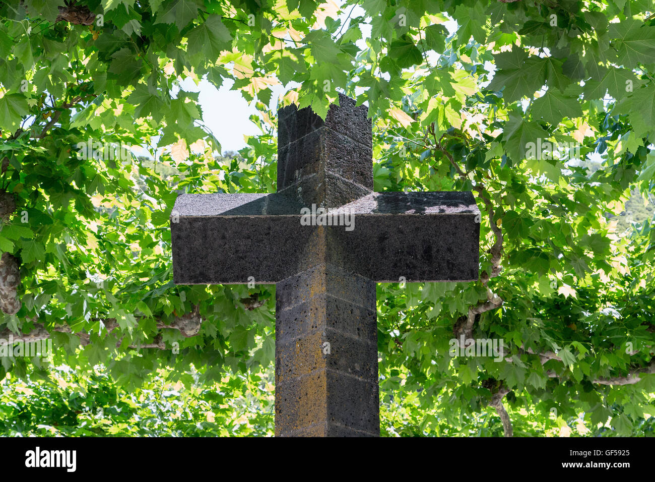 Katholisches Kreuz, aus vulkanischem Gestein, aus Basalt. Religiöses Wahrzeichen im Dorfzentrum von Lajes. Hintergrund gefüllt mit grünen Ahornblättern. Pico Azoren Stockfoto
