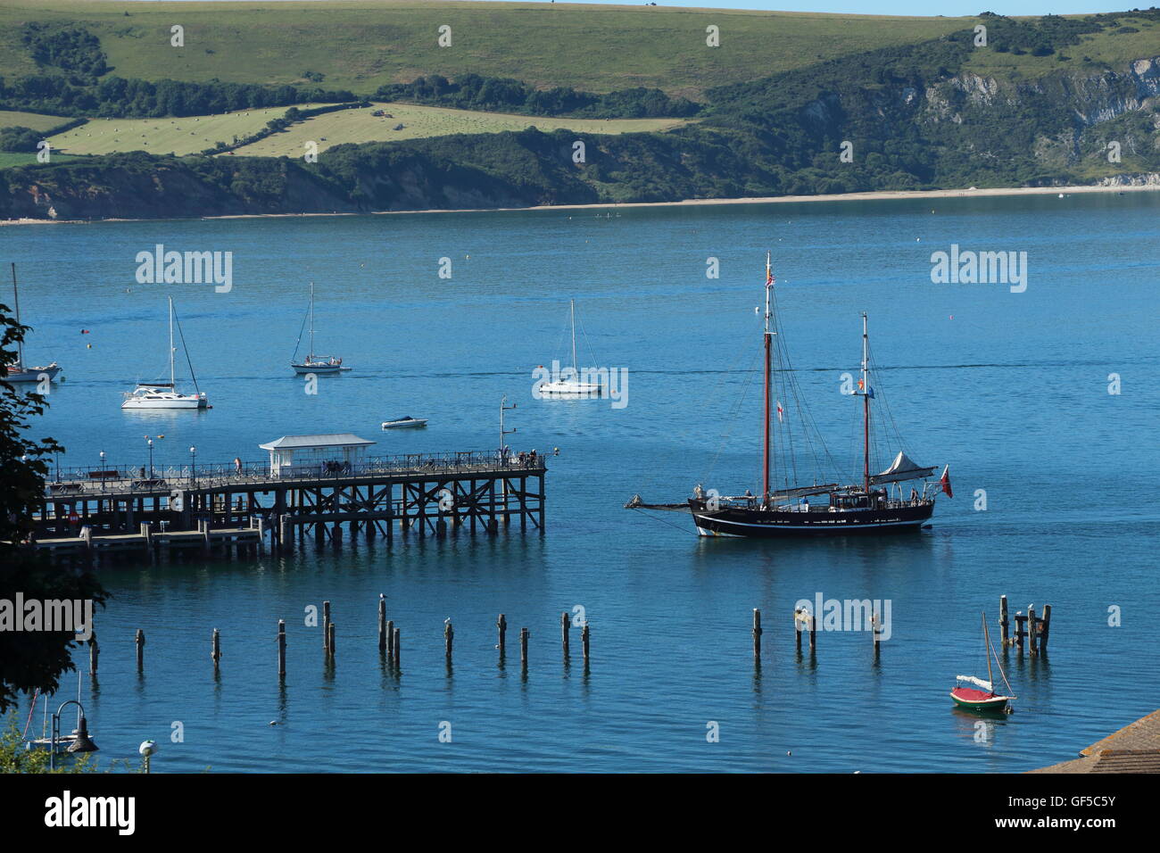 Segelboot in dock in Swanage Pier. Blaues Meer mit Ballard Down im Hintergrund Stockfoto