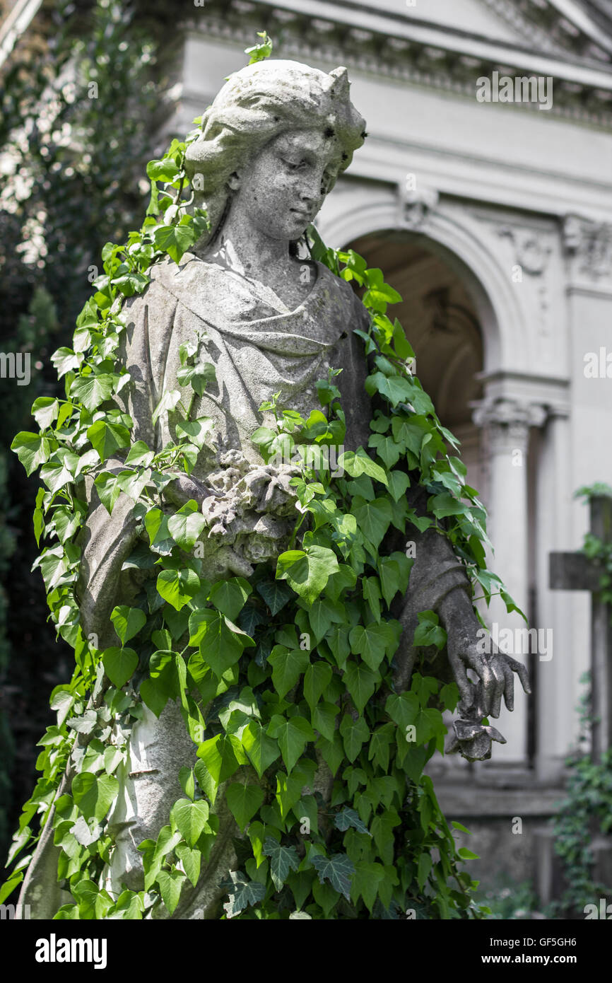 Eine betende Statue Frau bedeckt mit kriechenden Efeu in einem alten Friedhof. Stockfoto