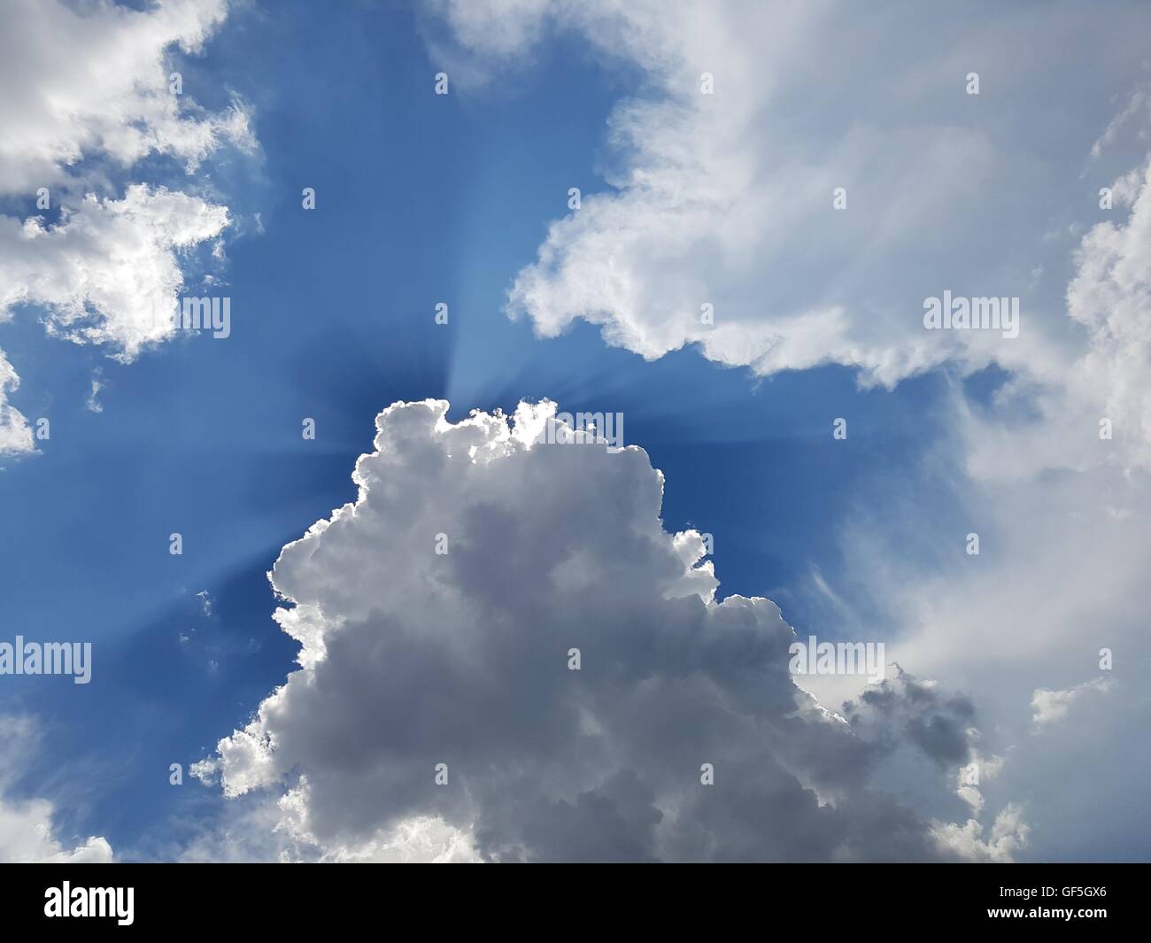 Cumulus-Wolken mit Lichtstrahlen auf blauem Himmel verteilen Stockfoto