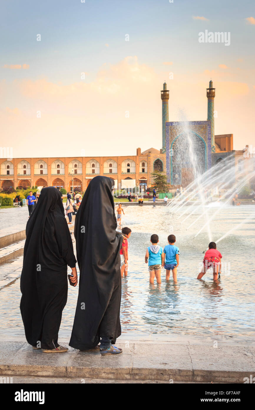 Frauen im Tschador betreuen ihre Kinder spielen mit Wasser bei Sonnenuntergang in Naqsh-e Jahàn Quadrat, Isfahan, Iran. Stockfoto