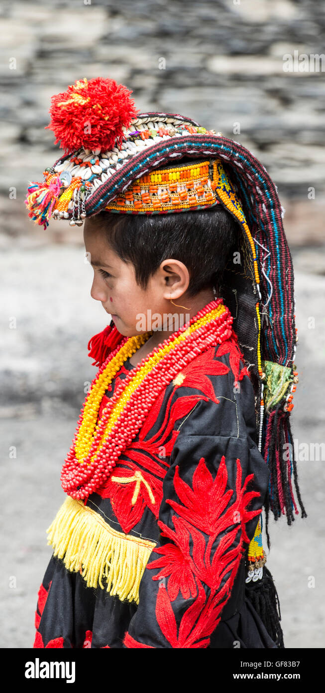 Kalash Mädchen trägt einen traditionellen Kopfschmuck verziert mit Kaurimuscheln und einem schwarzen bestickten Kleid Stockfoto