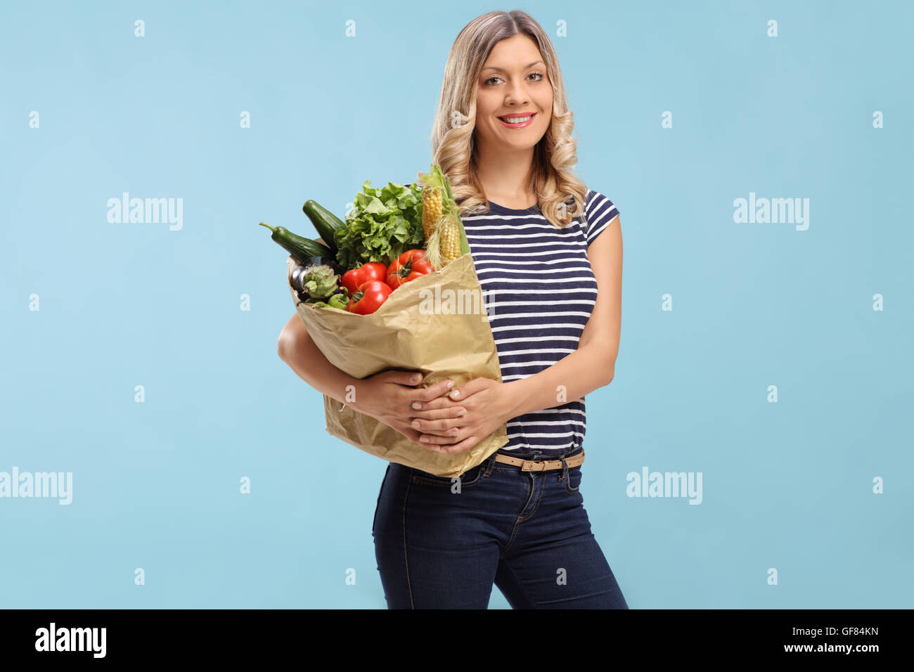 Junge Frau hält eine Einkaufstüte und schaut in die Kamera auf blauem Hintergrund Stockfoto
