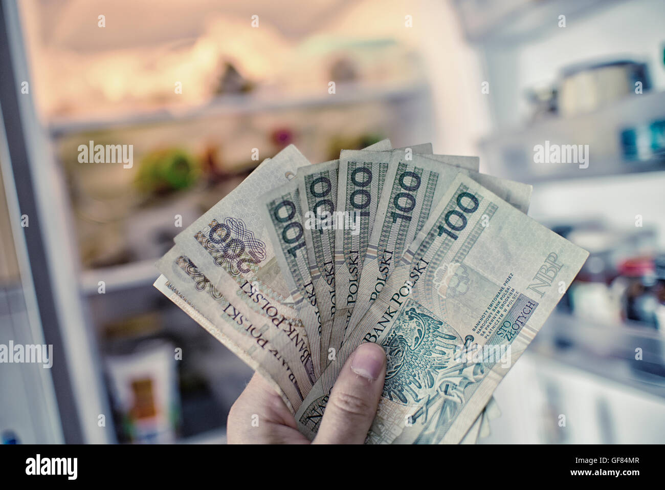 Hand mit PLN Geld vor offenen Kühlschrank Stockfoto