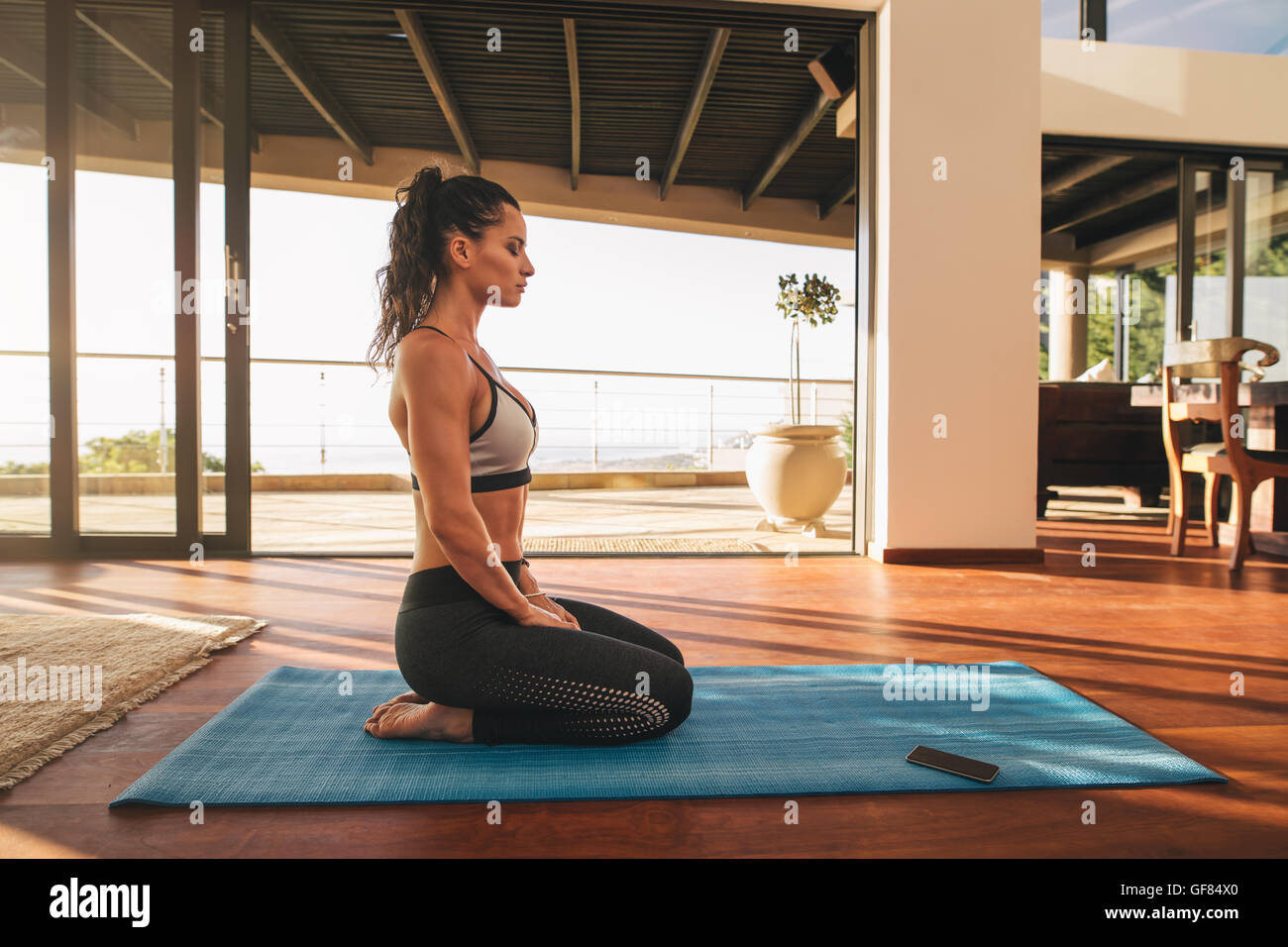 Blick Richtungskontrolle Fitness Frau sitzen im Yoga zu Hause darstellen. Weibchen in Sportbekleidung tun Meditation über Gymnastikmatte in lebenden ro Stockfoto