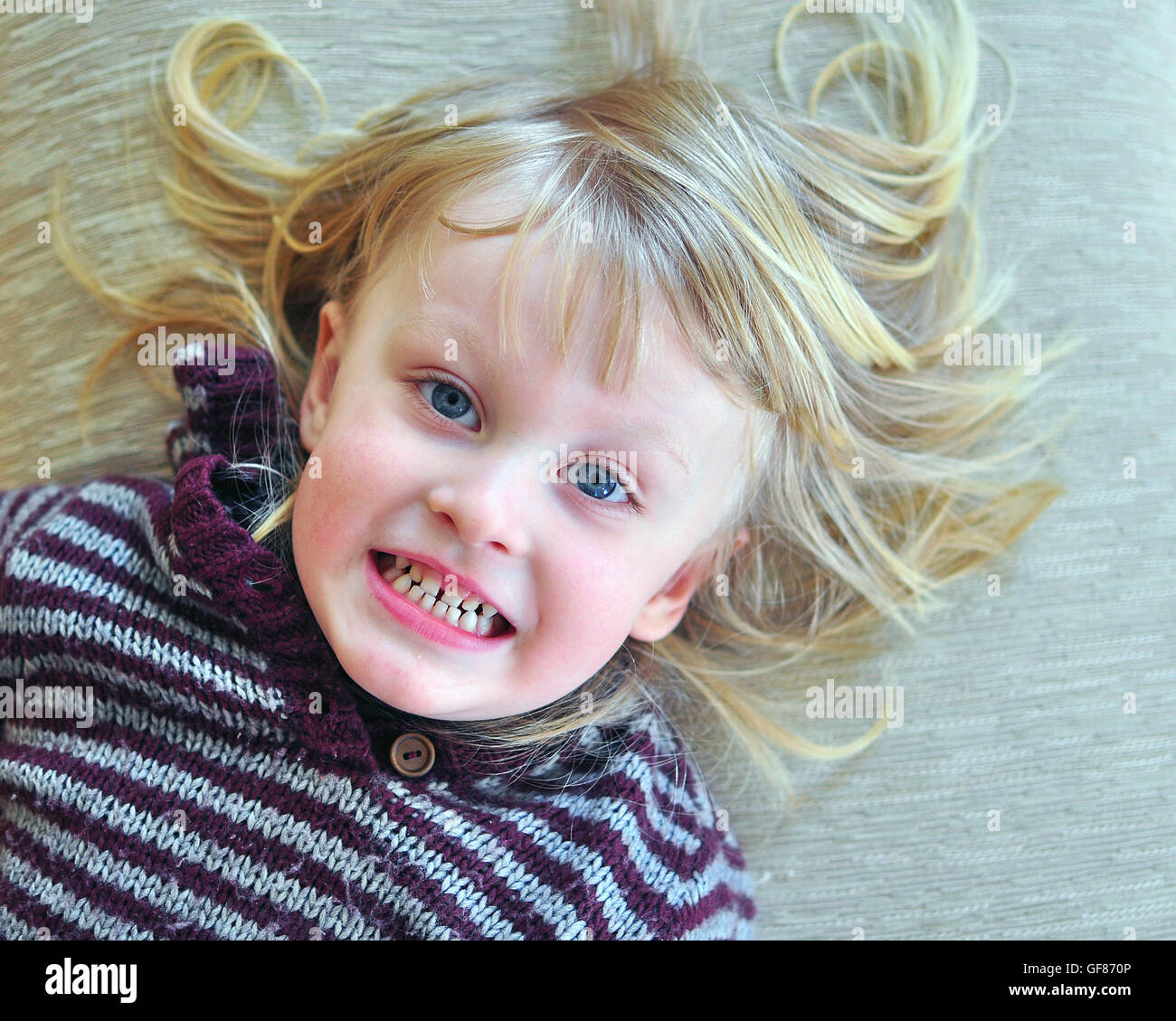 Süß lächelnden Baby mit einer langen blonden Haare auf dem Bett liegend Stockfoto