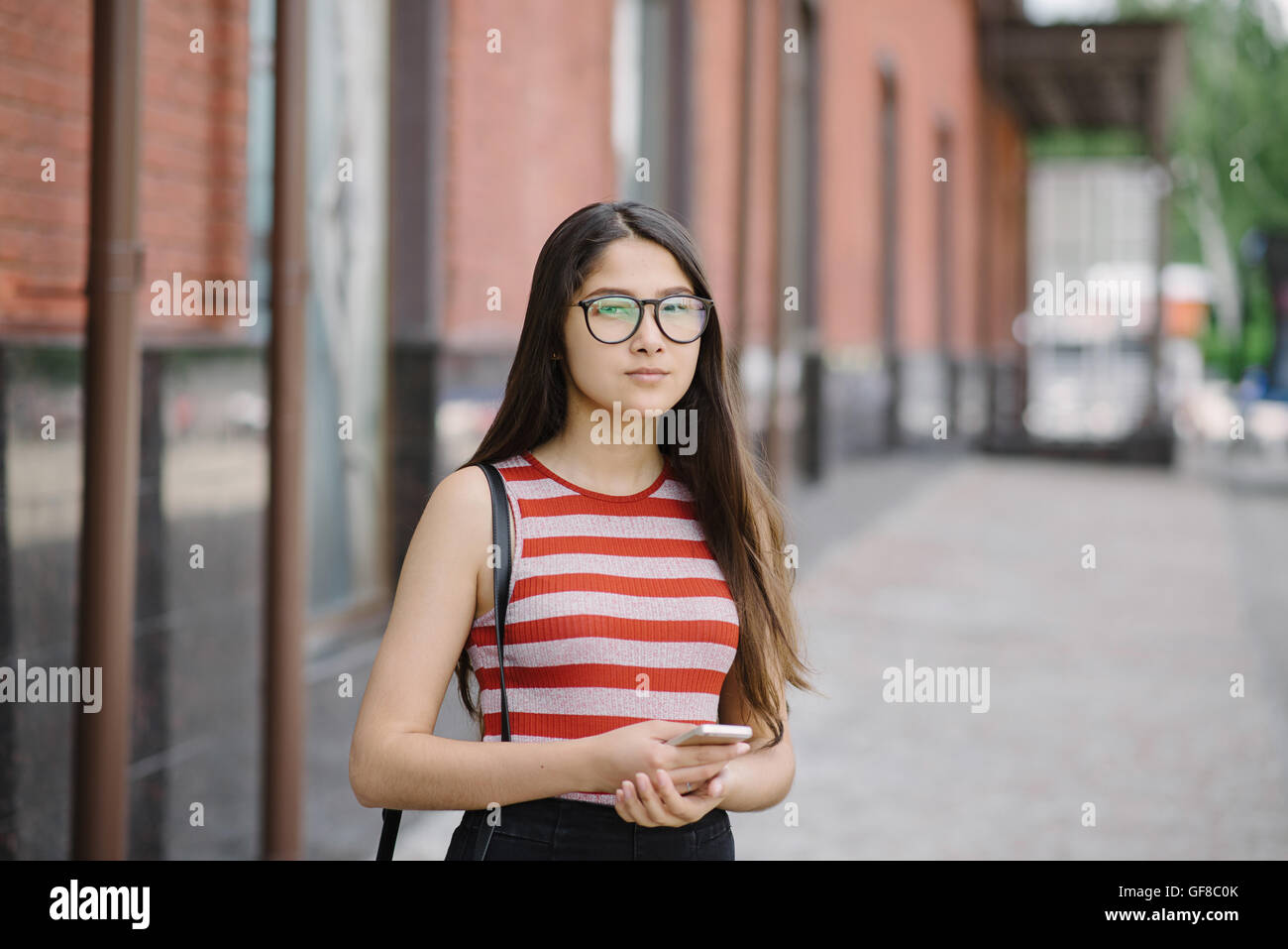 Junge asiatische Frau mit Brille Smartphone in Händen halten. Junge Frau auf Stadt Hintergrund. Stockfoto