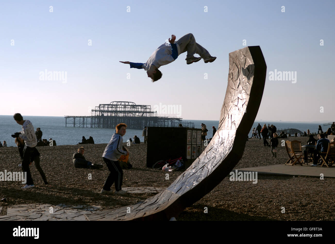 Ein Jugendlicher führt einen spektakulären Rückschlag auf einem der durch Die großen Skulpturen am Brighton Beach heute, wenn die Massen es genießen Die Wintersonne Stockfoto