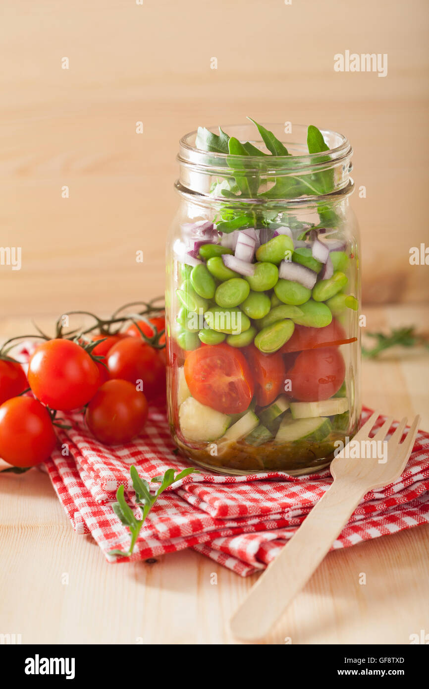 gesunder Gemüsesalat im Einmachglas: Tomaten, Gurken, Sojabohnen, Zwiebeln Stockfoto